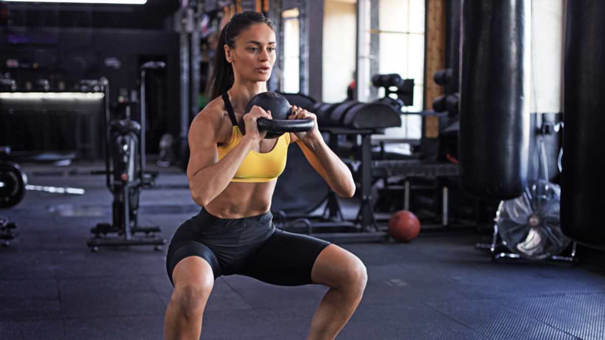 Image Of A Fit Woman In A Gym Squatting With A Kettlebell To Strengthen Tendons And Ligaments