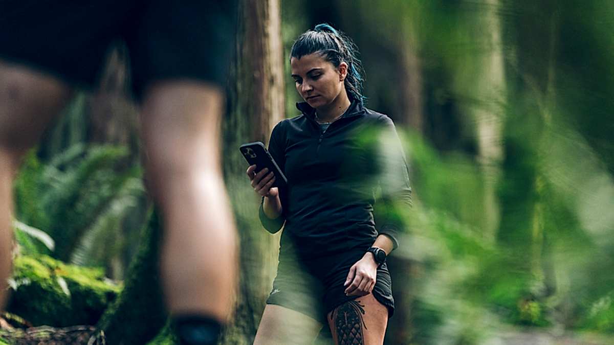 Image Of A Young Female Runner In The Woods Stopping On The Trail To Look At Her Phone To Check On Trainingpeaks Coach Payments